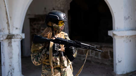 Caucasian woman in a protective suit with a machine gun. A female soldier in a camouflage uniform...