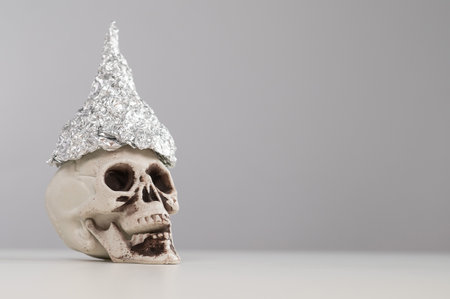 Plastic skull in a tinfoil cap on a white background. Copy space.の写真素材