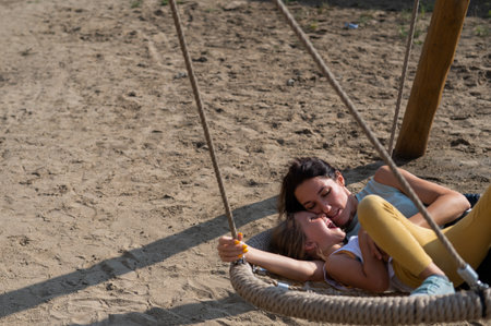 Mom and daughter swing on a round swing. Caucasian woman and little girl have fun on the playground.の写真素材