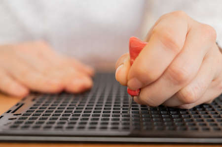 A woman uses a special stencil and stylus to write a letter in braille.