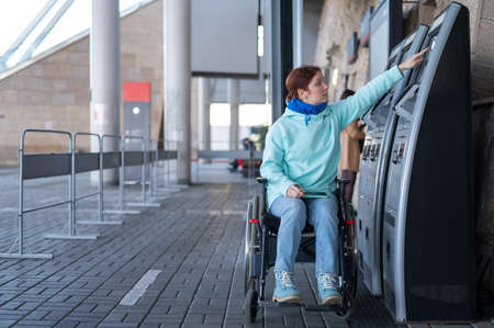 Caucasian woman in a wheelchair buys a train ticket at a self-service checkout.