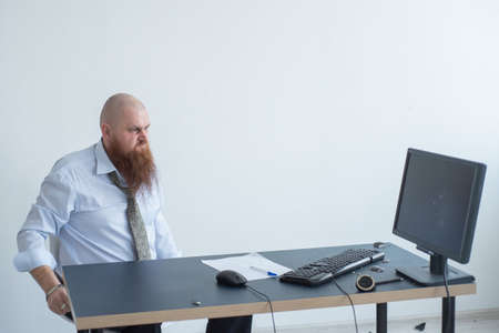 Angry bald man with a red beard in the office in a business suit crashes a computer. Manager with a nervous breakdown breaks the keyboard on the monitor.の写真素材