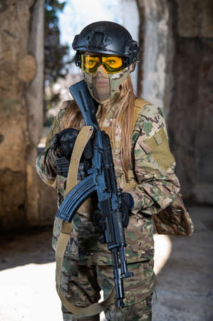 Portrait of a woman in a helmet and goggles with a machine gun in her hands. A female soldier in a camouflage uniform holds a weapon.の写真素材