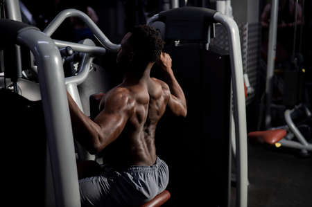 Shirtless african american man doing back exercises on a machine in the gym.の写真素材