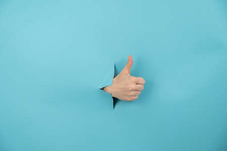 A womans hand sticking out of a hole from a blue background shows a thumbs up.の写真素材