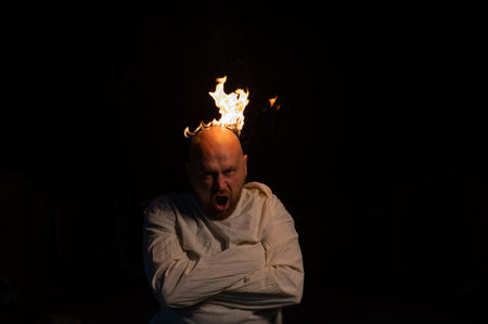 Bald man in a straitjacket with a burning head on a dark background.
