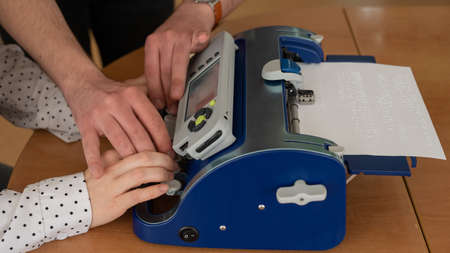 A man teaches a blind woman to type on braille machine.