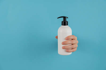 A womans hand sticks out of a hole in a blue paper background and holds a skin lotion pump.の写真素材