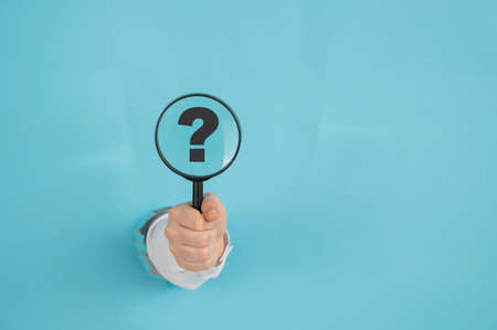 A womans hand sticking out of a hole on a blue paper background holds a magnifying loupe with a...