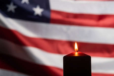 Burning candle against the background of the waving flag of the united states of america in the dark.の写真素材