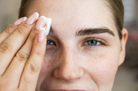 The master processes the eyebrows of a Caucasian woman with a cotton pad before laminating the...
