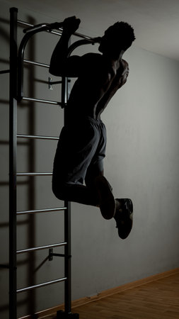 African american man with naked torso pulls up on horizontal bar in gym.の写真素材