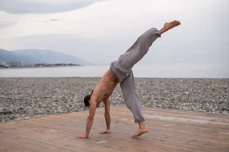 Shirtless caucasian man doing acrobatic wheel on the beach.