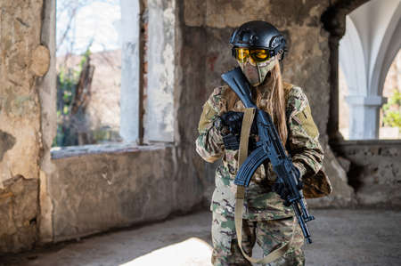 Portrait of a woman in a helmet and goggles with a machine gun in her hands. A female soldier in a camouflage uniform holds a weapon.の写真素材