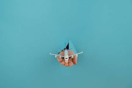 A female hand sticking out of a hole from a blue background holds a model of an airplane.の写真素材