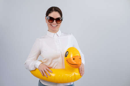 Caucasian woman in a white shirt dreaming of a vacation and wearing sunglasses and an inflatable duck.の写真素材