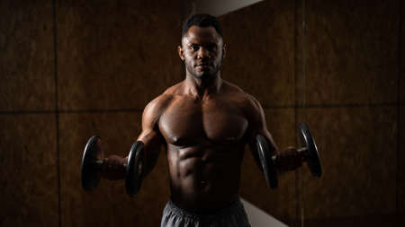 Muscular dark-skinned man doing an exercise with dumbbells.の写真素材