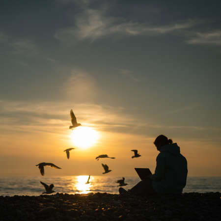 Caucasian woman typing on a laptop on the seashore at sunset. Freelance work.