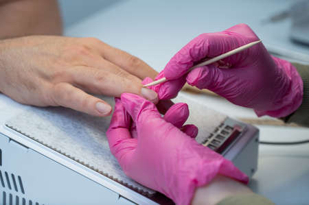 Manicurist removes cuticles with an orange stick to a male client.