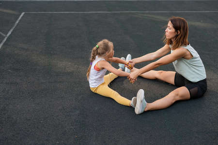 Mother and daughter go in for sports outdoors. Caucasian woman and little girl are engaged in fitness at the stadium.の写真素材