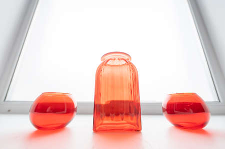Three empty glass red vases on the windowsill.