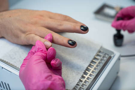A man on a manicure procedure paints his nails black in a beauty salonの写真素材