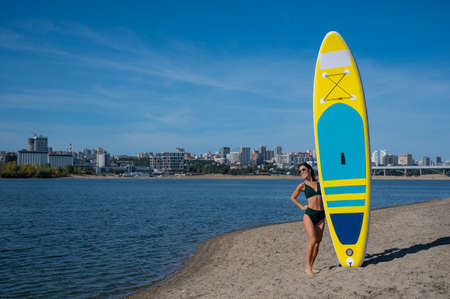 Caucasian woman walks along the beach and carries a sup board on the river in the city. Summer sport.の写真素材