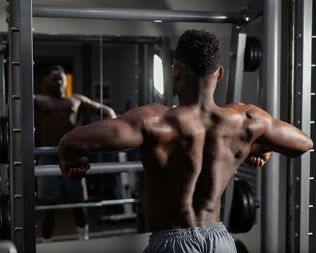Handsome afro american man posing showing back muscles in gym.