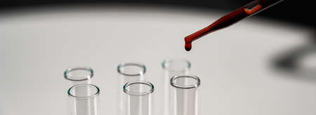 Close-up of a laboratory assistant dripping blood from a pipette into a test tube.