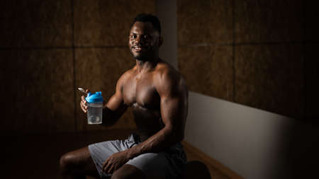Shirtless african american man drinking from a shaker in the gym.の写真素材