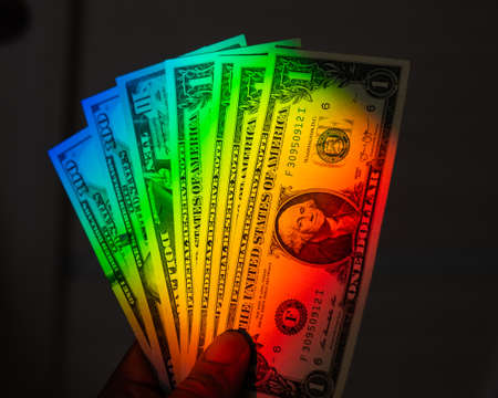 Rays of a rainbow on a mans hand with a bundle of dollars.の写真素材