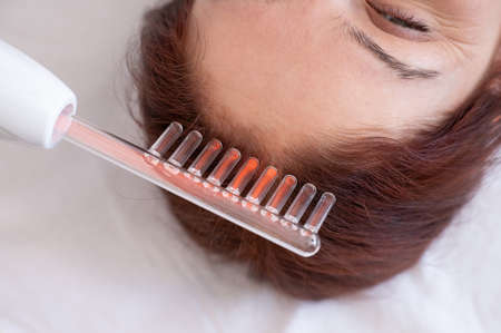 Caucasian woman on a hair care procedure using the Darsonval apparatus.