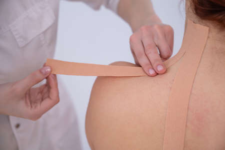 Female doctor glues kinesio tapes on the patients shoulder.の写真素材