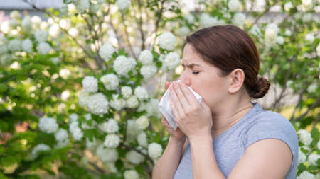 Caucasian woman suffers from allergies and blows her nose into a napkin while walking in the park.の写真素材