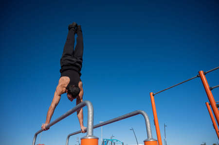 Shirtless man doing handstand on parallel bars at sports ground.の写真素材