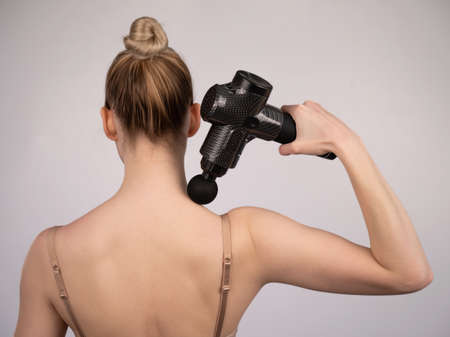 Caucasian woman giving herself a back massage with a gun.の写真素材