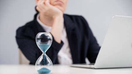 Business woman is bored at work and looks at the hourglass.