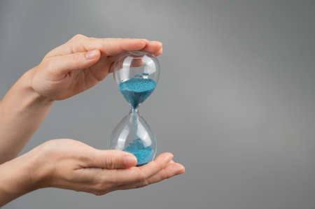 Woman holding an hourglass on a gray background. Close-up. Copy space.の写真素材
