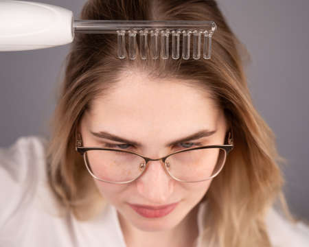 Caucasian woman combing her hair with a darsonval device.