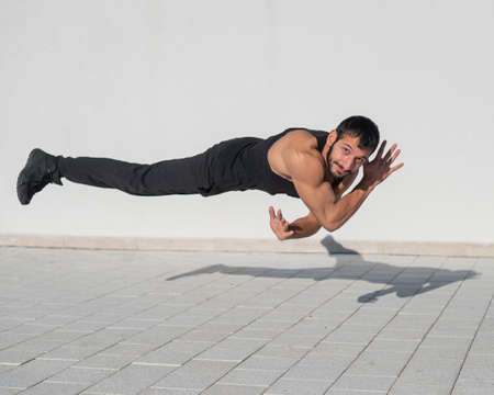 A man in black sportswear jumps while doing push-ups outdoors.