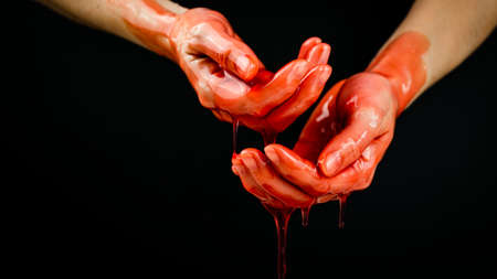 Womens hands in a viscous red liquid similar to blood.