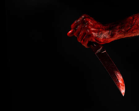 Man holding knife with bloody hand on black background.