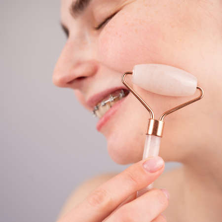 Close-up portrait of a woman uses a quartz roller massager to smooth wrinkles on her forehead.の写真素材