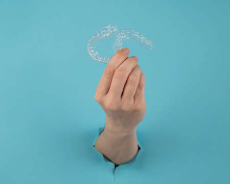 A female hand sticking out of a hole from a blue background holds removable night retainers.の写真素材