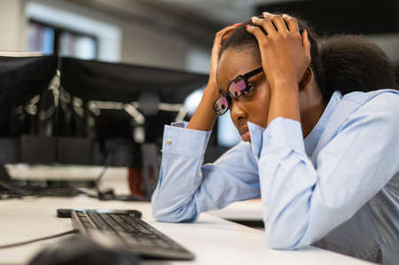 African young woman sitting at her desk clutching her head.の写真素材