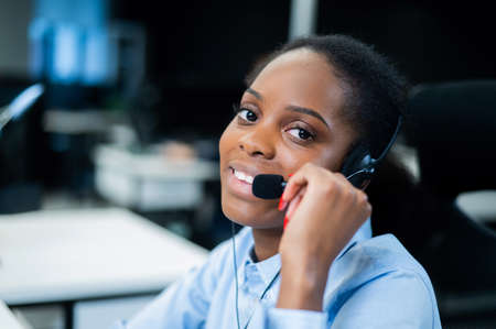 African young woman talking to a client on a headset. Female employee of the call center.