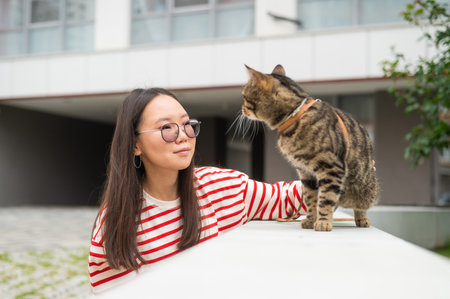 A striped cat sits on a bench outdoors. Young woman walking with her pet outdoors.の写真素材