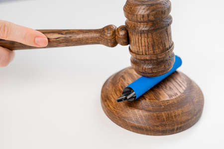Judge hammering disposable vape with referees gavel on white table.