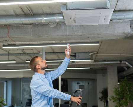 Caucasian bearded man repairing the air conditioner in the office.