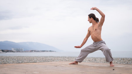 Caucasian man with naked torso practicing wushu on the seashore.の写真素材